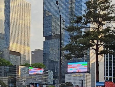 하트 모양 창 너머로 보이는 강남의 고층 빌딩과 소나무, 전광판